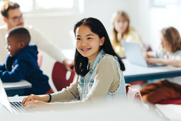 Happy Asian girl enjoying a coding class, using a laptop to engage in the lesson