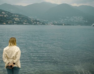 Fototapeta na wymiar Photo session of a girl on the background of a lake overlooking the mountains. Italy, Como, May 2023.