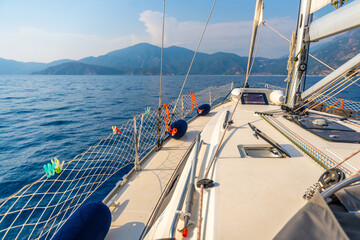 Yacht sailing in an open sea. Close-up view of the deck, mast and sails. Clear sky, waves and water splashes