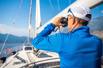 Young man captain on the yacht looking through binoculars during sailing boat control. Travel and active life.