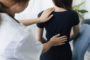 Doctor is diagnosing female patient with back pain in examination room at hospital.