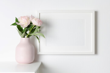 Frame mockup on white wall with pink peony flowers, mockup for artwork, photo or print presentation