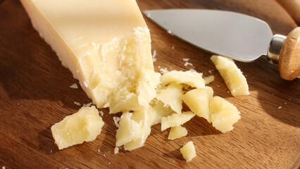 Hard cheese with a knife on a cutting board. Wooden background. Parmesan with broken pieces. Traditional Italian cheese grana parmigiano reggiano. Close-up. - obrazy, fototapety, plakaty