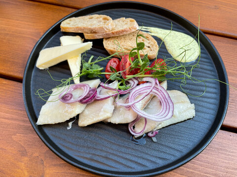Plate with marinated herring matjes fish filets with onion rings, butter, tomatoes and bread slices high angle view