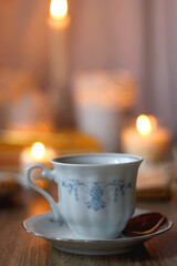 Cup of tea or coffee, plate of cookies, books, e-reader, pencil and lit candles on the table. Selective focus.