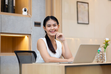 Female looking at camera.  Young Asian business working woman work online job on laptop computer at smallbusiness home office. Work from home