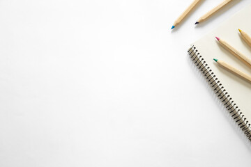 Wooden pencils of different colors and a notebook on a white background.
