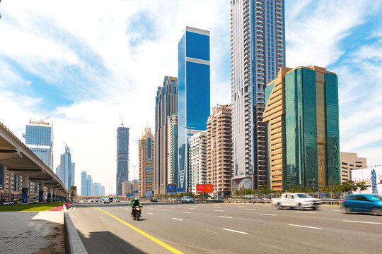 Dubai, United Arab Emirates - April 20th 2023: View into the Sheikh Zayed Road with skyscrapers and cars on the road. Blue sky with clouds. Overhead railway station on the left side.