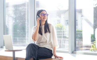 Cheerful young woman in glasses talking on a smartphone in the office.