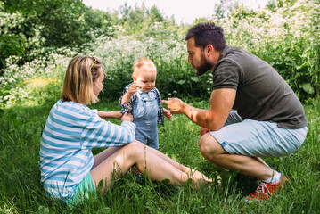 Naklejka na ściany i meble Mom, dad and little son spend time together in the summer outdoors