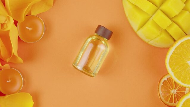 Jar of cosmetic oil perfume on the table . Composition of citrus slices, flowers, mango, aroma candles on orange background close-up, top view, zoom. Summer bright texture studio shot.