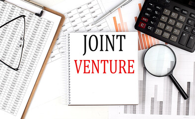 JOINT VENTURE text on notebook with clipboard and calculator on a chart background