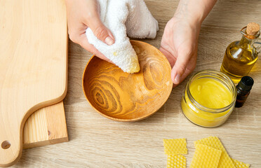 Woman hands apply homemade beeswax wood treatment polish to restore natural wood bowl color....