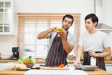 Happy cheerful LGBTQ+ gay romantic couple preparing and making their breakfast together in the...