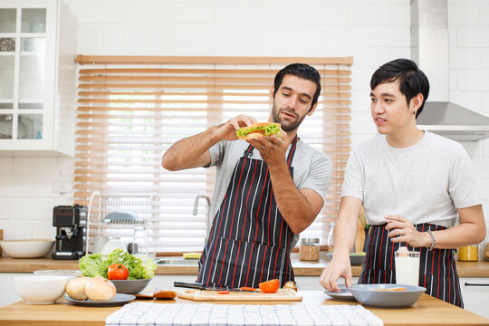 Happy cheerful LGBTQ+ gay romantic couple preparing and making their breakfast together in the kitchen. Diversity in ethnicity, nationality, and sex concept. LGBTQ+ married people lifestyles. - Powered by Adobe