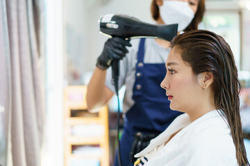 Happy cheerful Asian beautiful woman having a haircut and styling in professional hairdresser - salon shop, female hairdresser using a hair dryer bowling female customer hair.