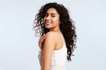 A model girl with glowing skin and thick black and curly hair looks over her shoulder at the camera...