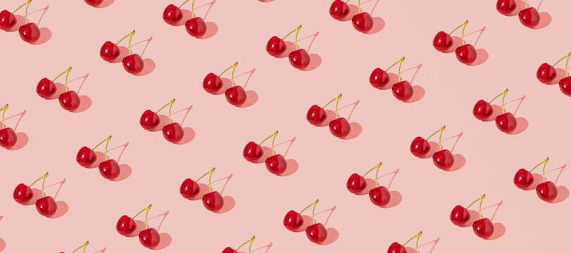 Fresh juicy cherries, creative fruit pattern, dusty rose pink background. 