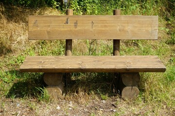 Braune Holzbank auf Wiese vor Bäumen im Wald bei Sonne am Mittag im Sommer