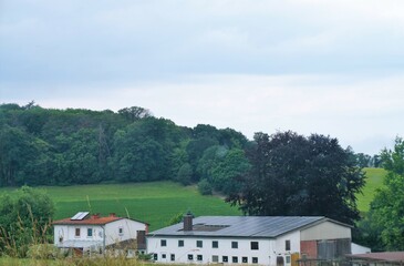 Fototapeta na wymiar Grüne Landschaft Panorama mit Bauernhof vor Berghügel mit grünen Feldern und Wald vor Himmel bei Sonne am Mittag im Sommer