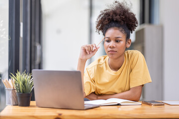 Business And Education Concept. Smiling african american  sitting at desk working on laptop writing letter in paper documents, free copy space. Happy millennial female studying using laptop	