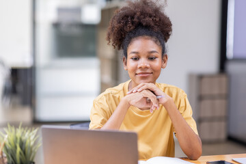 Business And Education Concept. Smiling african american  sitting at desk working on laptop writing letter in paper documents, free copy space. Happy millennial female studying using laptop	