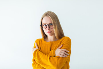 Portrait of young attactive blondie woman in eye glasses looking at camera. Girl hug herself in yelow sweater
