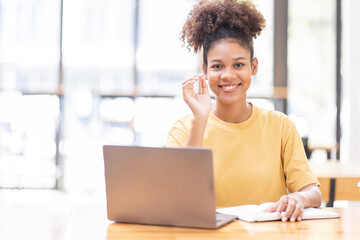 Business And Education Concept. Smiling african american  sitting at desk working on laptop writing letter in paper documents, free copy space. Happy millennial female studying using laptop	