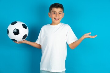 Little hispanic boy wearing white T-shirt holding a football ball 