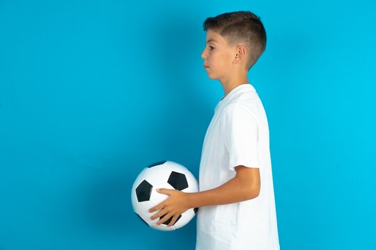 Little hispanic boy wearing white T-shirt holding a football ball looking to side, relax profile pose with natural face with confident smile. - Powered by Adobe