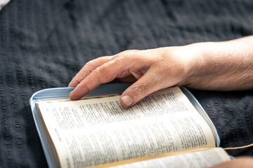 An elderly woman reads a book of the Bible, hands and close-up.