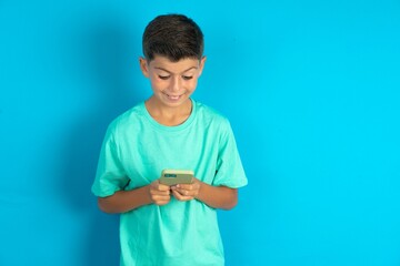 Little hispanic boy wearing green T-shirt using mobile phone chatting free time .