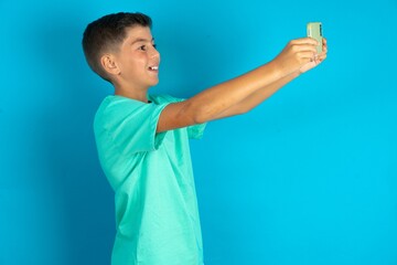 Little hispanic boy wearing green T-shirt taking a selfie to post it on social media or having a...