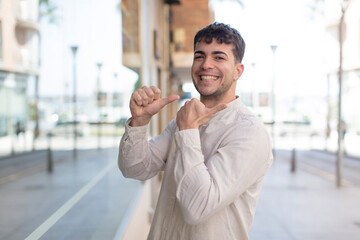 young handsome man smiling cheerfully and casually pointing to copy space on the side, feeling happy and satisfied