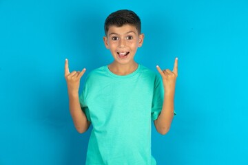 Little hispanic boy wearing green T-shirt makes rock n roll sign looks self confident and cheerful...