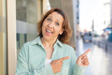 Fototapeta premium middle age woman smiling cheerfully and pointing to copy space on palm on the side, showing or advertising an object