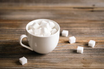 Cup with sugar cubes on a wooden surface, close-up.