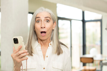 pretty senior woman feeling extremely shocked and surprised. smartphone concept