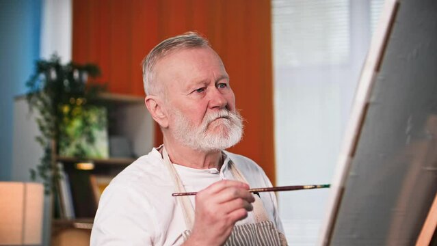 hobby retired, creative talented man enthusiastically draws a picture with paints and brushes at home