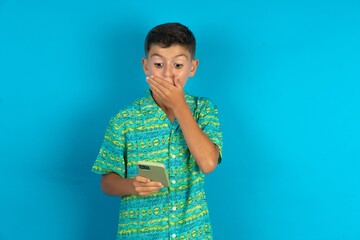 Little hispanic boy wearing green aztec shirt being deeply surprised, stares at smartphone display, reads shocking news on website, Omg, its horrible!