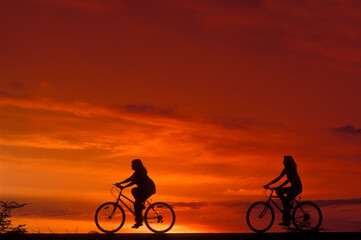 Fototapeta na wymiar Two teenage girls riding bicycles at sunset