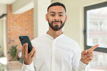young  adult man smiling cheerfully, feeling happy and pointing to the side. smartphone concept