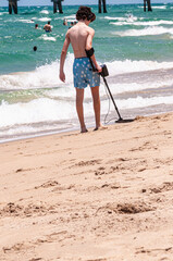 Back view of a young, adult male, using metal detector on, sandy shoreline of, Mediterranean sea