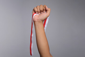Close-up hands of a man holding a red and white ribbon symbolize the Indonesian flag isolated on gray background. 17 August Indonesia independence day concept