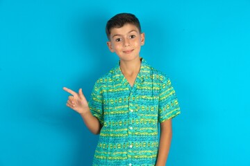 Little hispanic boy wearing green aztec shirt points to side on blank space demonstrates advertisement. People and promotion concept