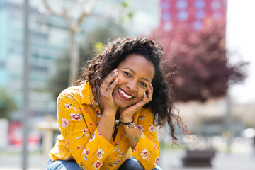 Fototapeta premium Beautiful young african woman sitting outside in the city