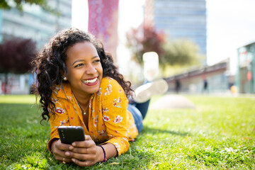 Smiling young black woman lying on grass with mobile phone