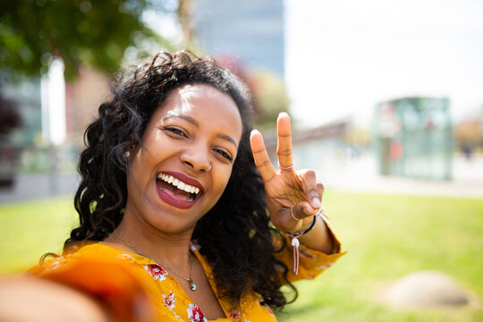 Cheerful young african woman taking selfie with peace sign outside