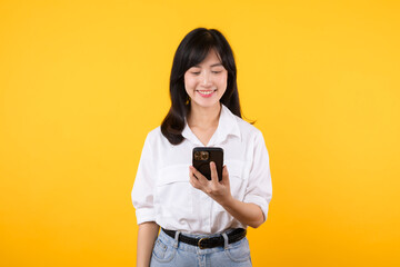 Portrait young asian woman happy smile wearing white shirt and denim jean plants using a smartphone isolated on yellow background. app smartphone concept.