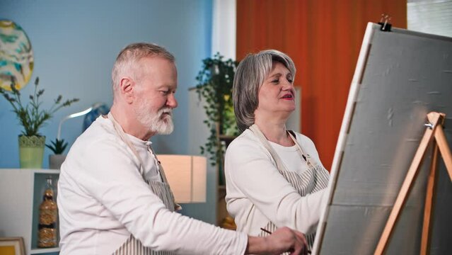 entertainment of elderly, talented old man and woman paint a picture with paints and brushes using an easel in a cozy room